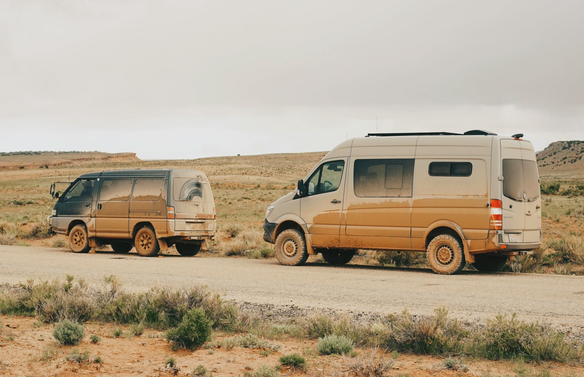 image of very muddy sprinter van next to a smaller mitsubishi van also covered in mud on the side of the road in utah