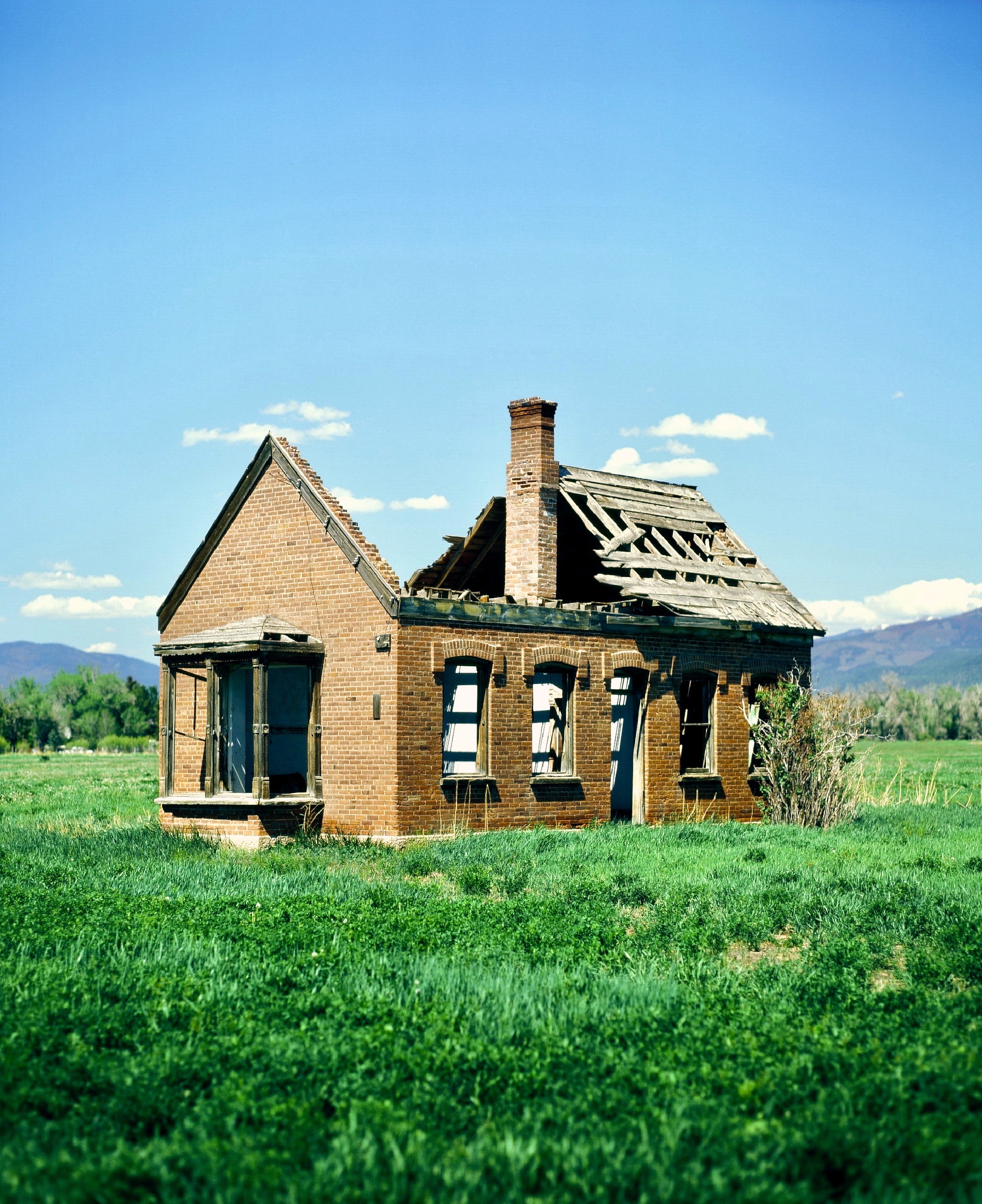 house in green field under a sunny sky with the entire roof blown off