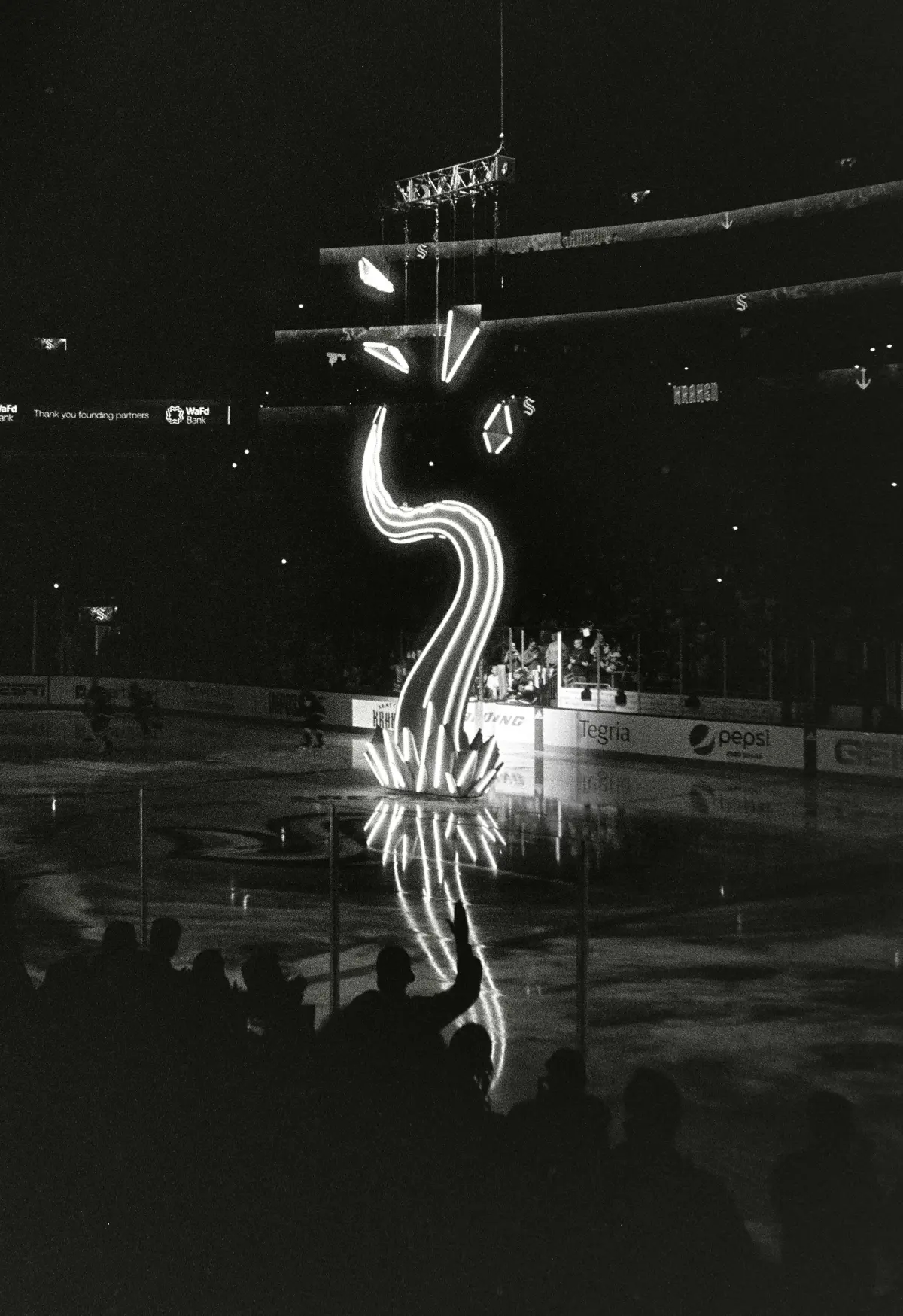 black and white grainy image of a neon light tentacle emerging from an ice hockey arena against a dark background