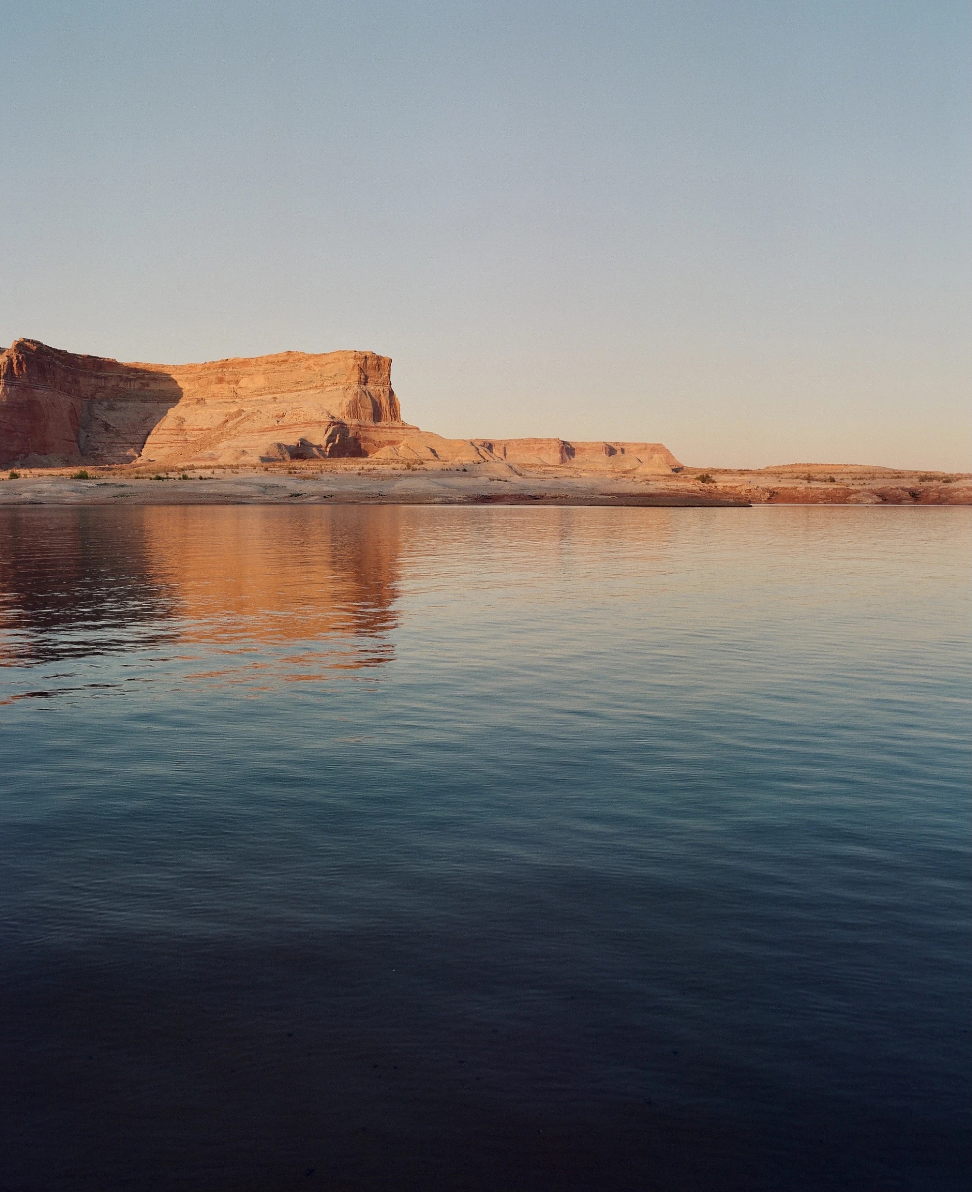 red rock cliff behind a body of water which has natural bands of color from the sky and cliff reflection